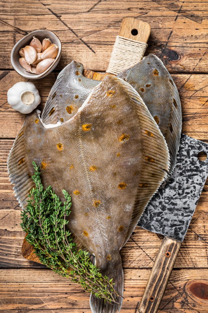 Raw flounder flatfish on butcher board with cleaver. wooden background. Top view